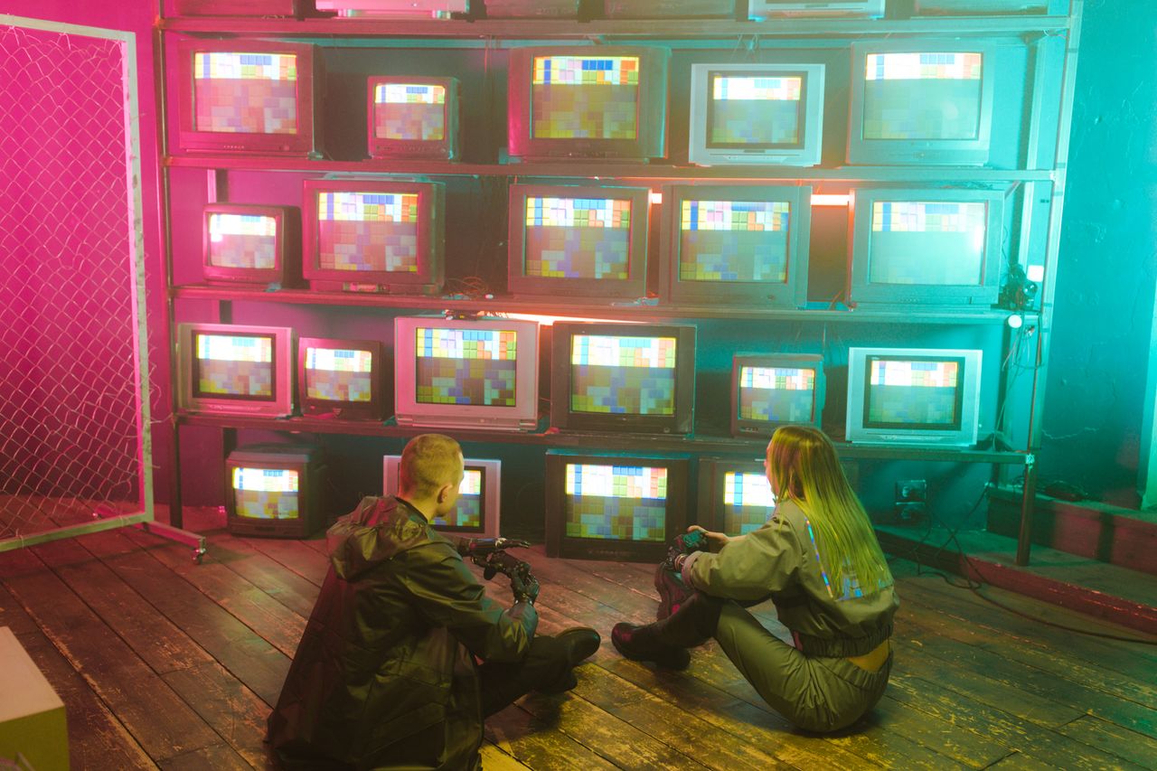 A cyberpunk inspired setting featuring two people with retro TVs displaying colorful test screens.